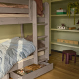 Cajones marrones FLEXA para debajo de la cama de la gama CLASSIC, con ropa de cama a rayas azules y estantes, con un diseño seguro para los niños en una habitación infantil.