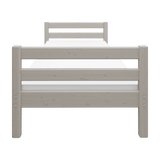 Cama individual FLEXA de la colección CLASSIC, en madera gris claro, mostrada en una habitación infantil con las barandillas visibles.