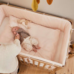 Woman beside FLEXA baby bed from OAK collection, light wood finish, in nursery with child-safe rounded edges visible.