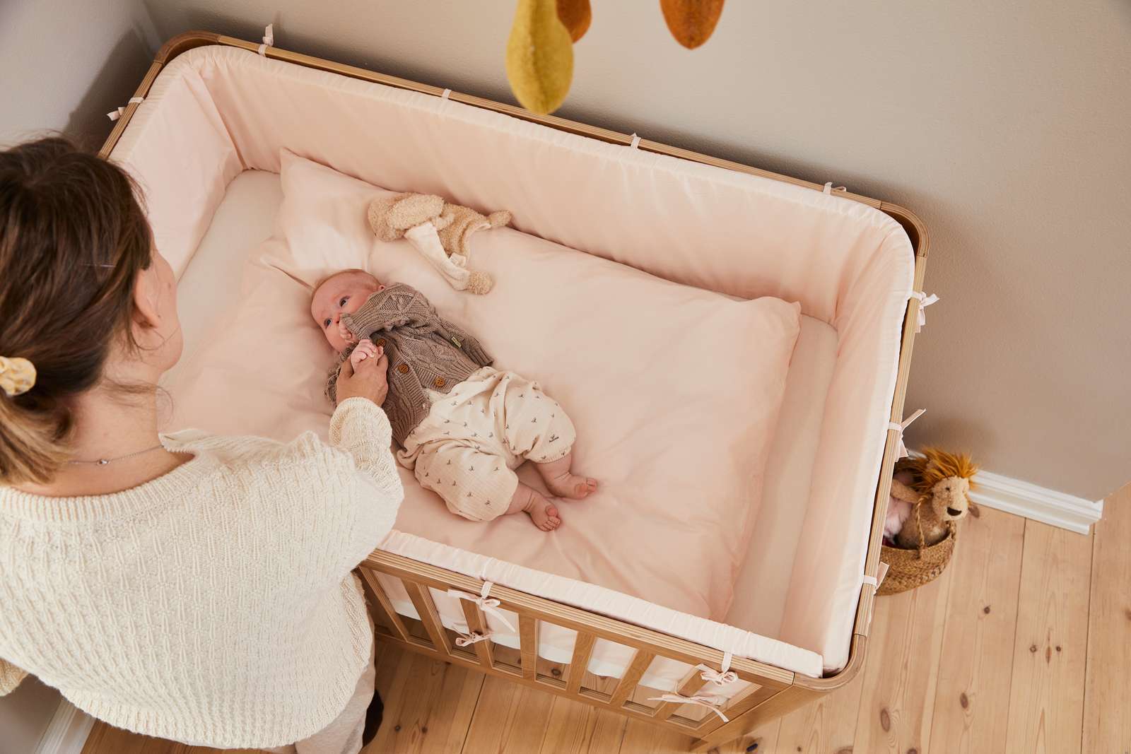 Mujer junto a una cuna FLEXA de la colección OAK, con acabado en madera clara, en una habitación infantil en la que se aprecian los bordes redondeados, seguros para los niños.