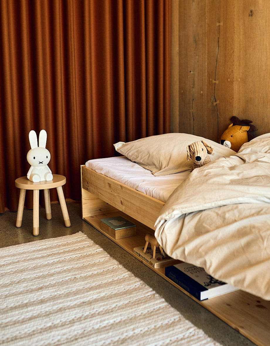 Taburete infantil FLEXA DOTS en rosa pálido, con un diseño apto para niños, en una habitación infantil con cama de madera y cortina naranja.