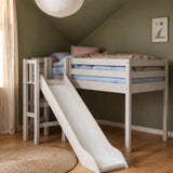 Cama alta FLEXA WHITE con tobogán y barandilla de seguridad de la colección CLASSIC en una habitación infantil verde, con suelo de madera, luminosa y apta para niños.
