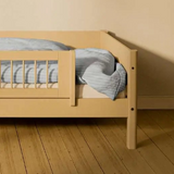 Barandilla de seguridad corta FLEXA SAND de WHITE & NOR en una cama infantil con ropa de cama a rayas azules en una habitación infantil de color beige.