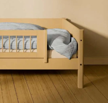 Barandilla de seguridad corta FLEXA SAND de WHITE & NOR en una cama infantil con ropa de cama a rayas azules en una habitación infantil de color beige.
